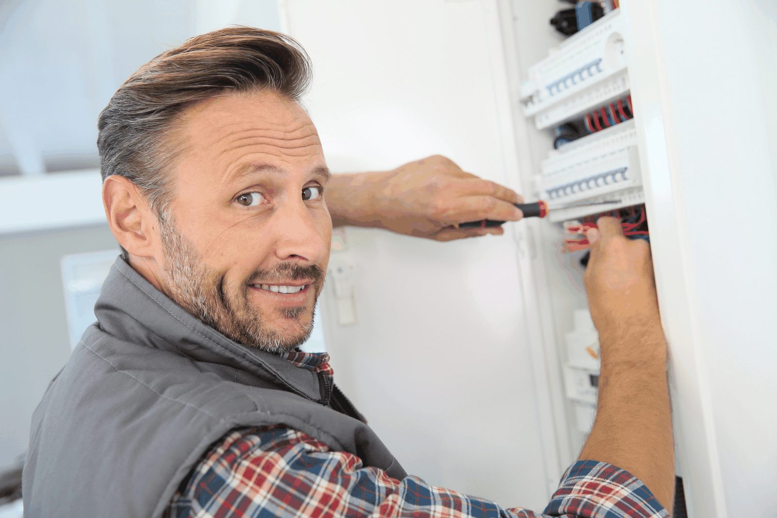 Smiling electrician working on a breaker panel with a screwdriver